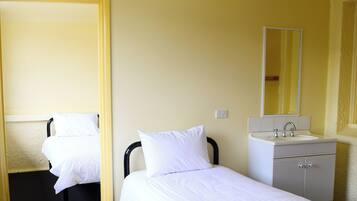 A hotel room with two single beds, a ceiling fan, a bathroom with a sink and mirror, and a door leading to another room.