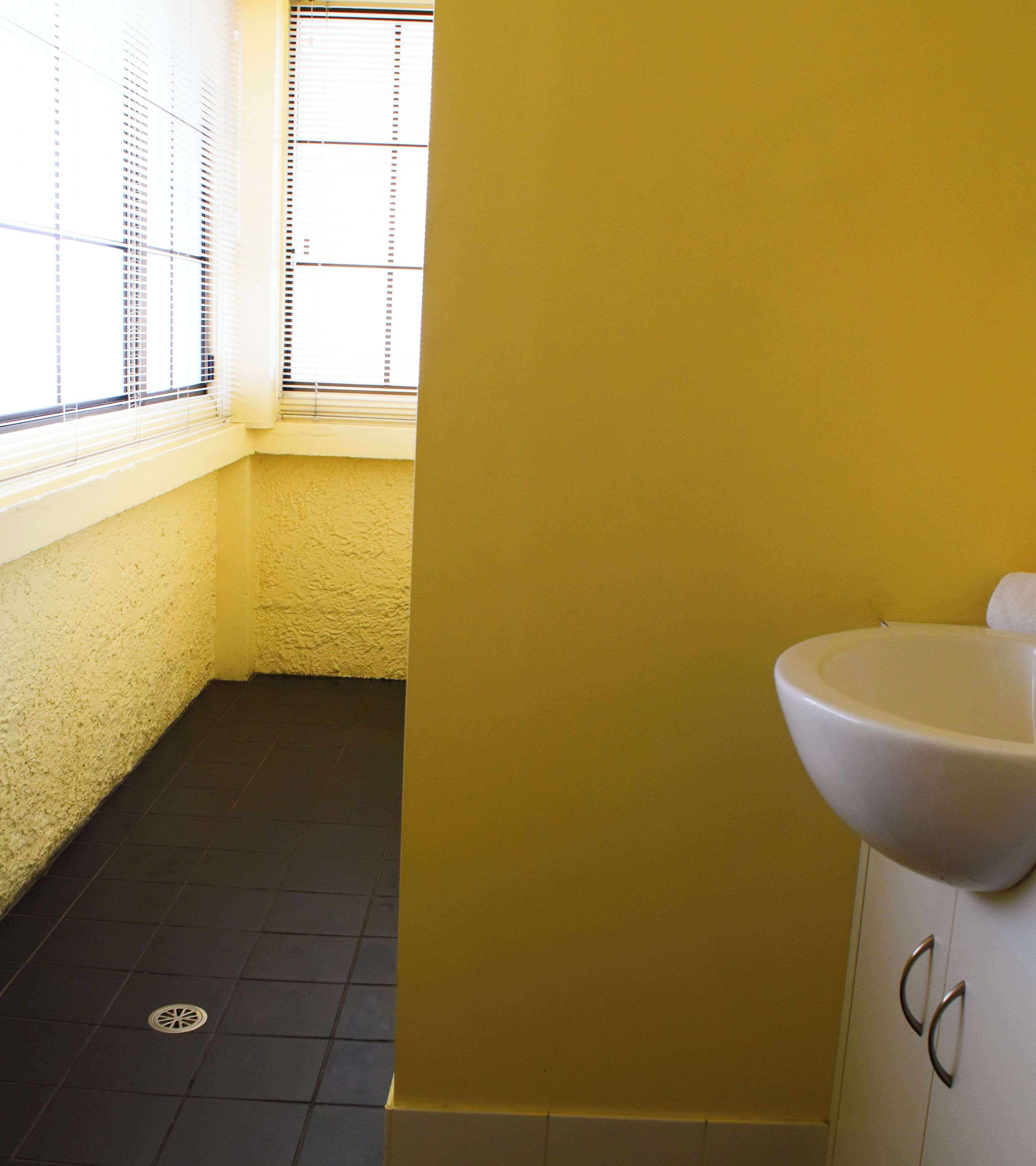 A bathroom with a yellow wall, a white sink, and a window with blinds.