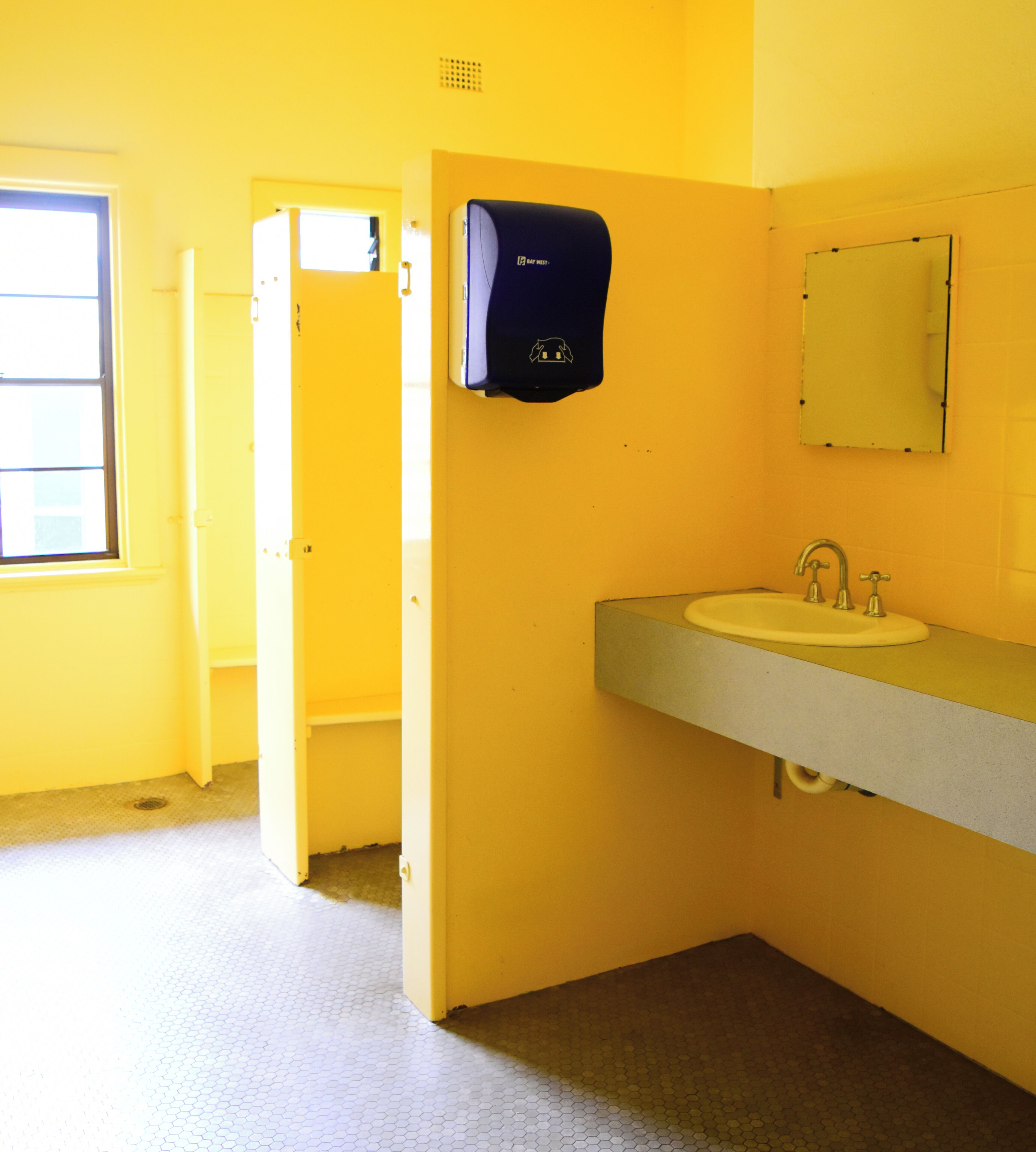 Un baño con pared amarilla, un lavabo con espejo y un dispensador de toallas de papel.