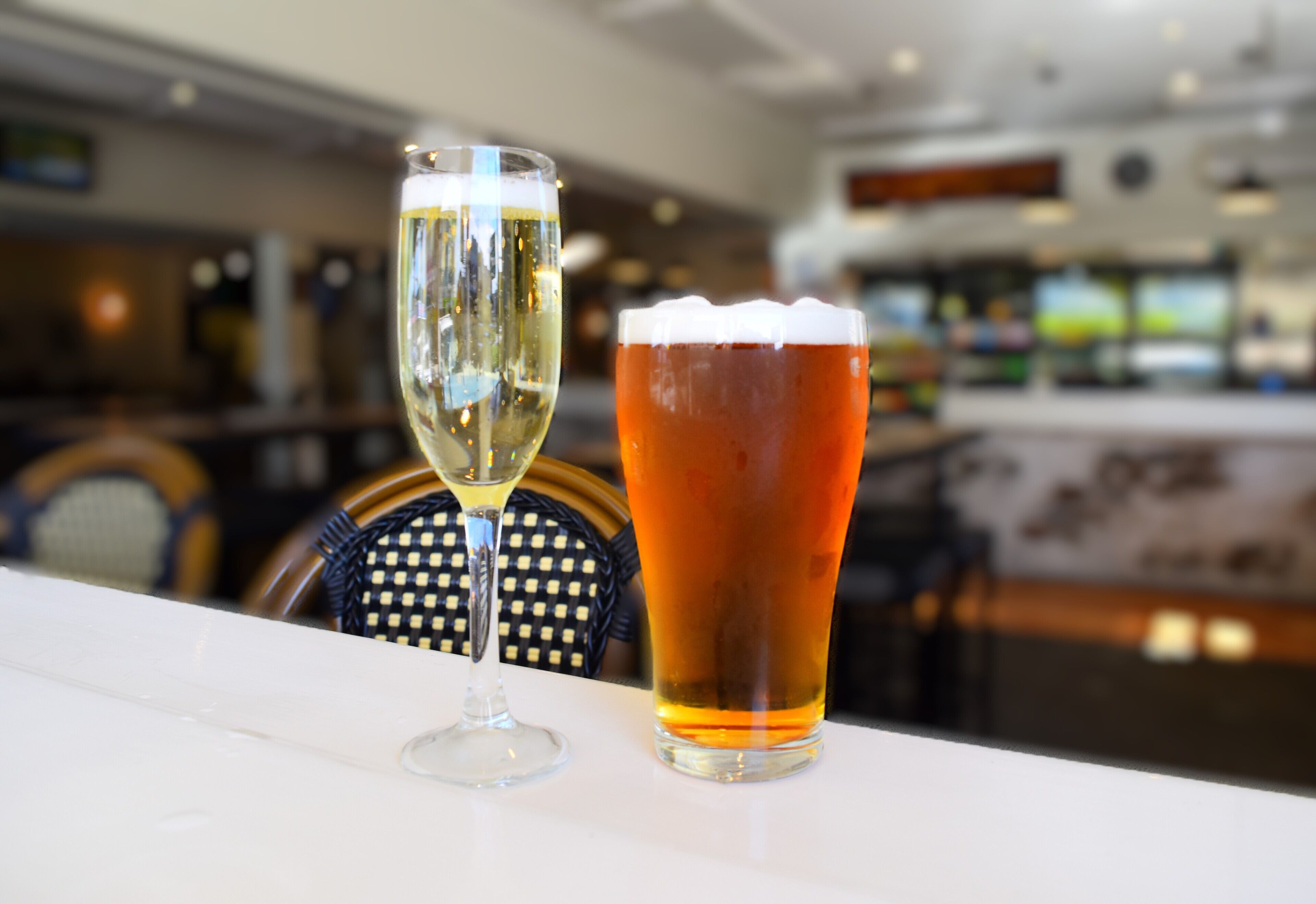 A bar setting with a glass of white wine and a glass of amber-colored beer on a white table.