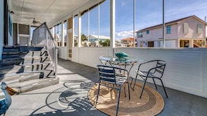 Un espace extérieur abrité, doté d’une table et de chaises, d’un escalier et de grandes fenêtres offrant une vue sur les bâtiments voisins.