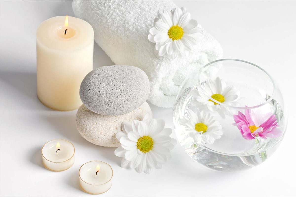 A spa setting with a lit candle, white towels, stones, and a glass bowl with flowers.