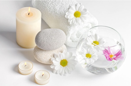 A spa setting with a lit candle, white towels, stones, and a glass bowl with flowers.