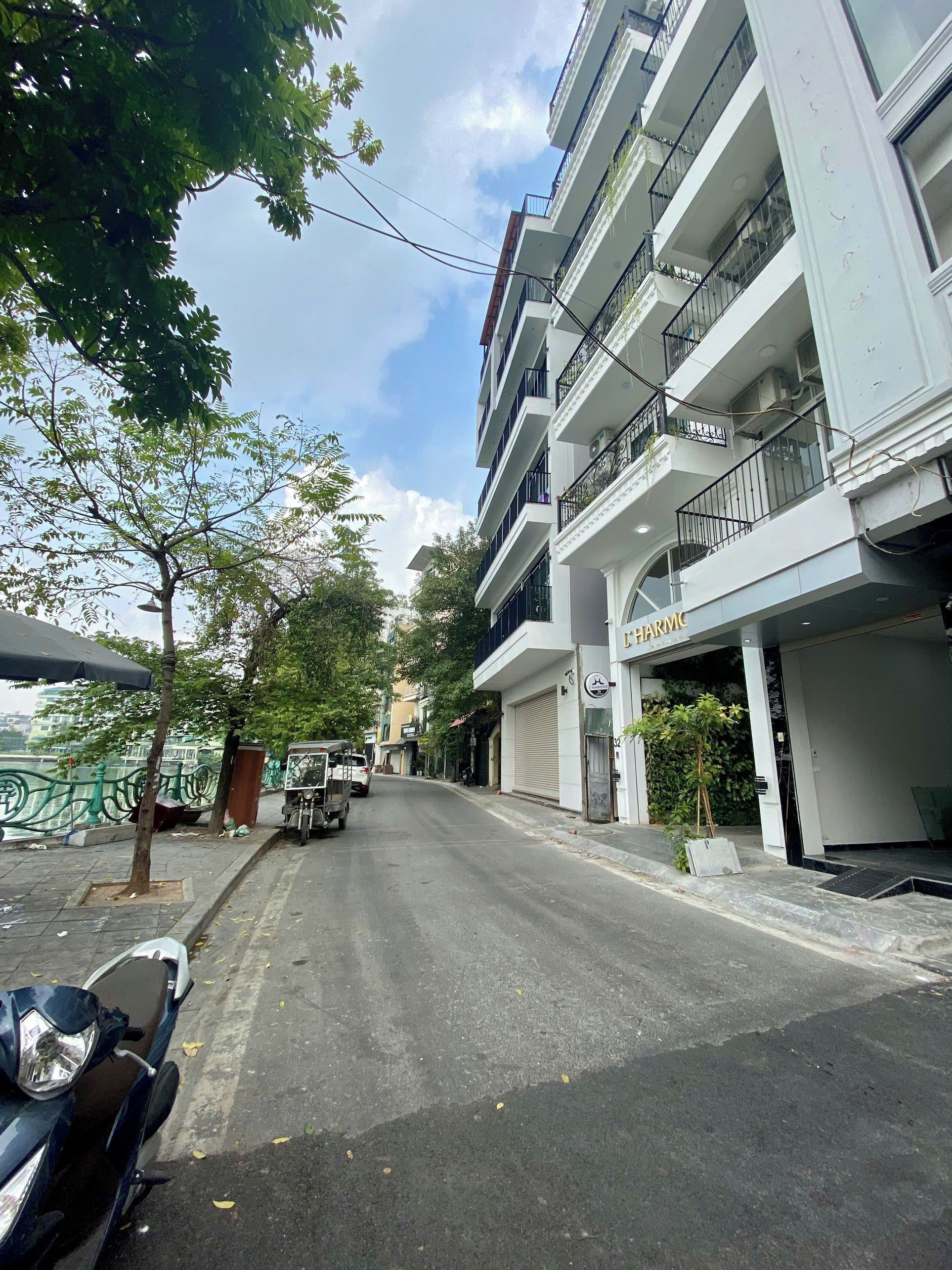 Um edifício de vários andares com varandas, uma motocicleta estacionada e uma rua arborizada.