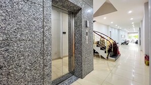 A modern hotel lobby with a granite elevator, a staircase with a red railing, and a clean, tiled floor. - NINE HOUSING 30 Yen Hoa (Hanoi)