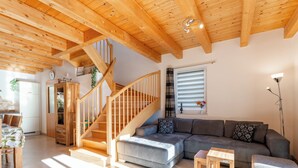 Een ruime woonkamer met een houten trap, een grijze bank en een eettafel.