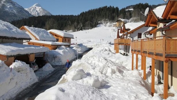Een besneeuwd dorpje met houten gebouwen, een skilift en een berg op de achtergrond.