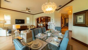 A modern living room with a dining area, a television, and a kitchen in the background.