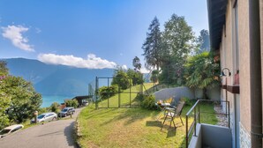 A view of a courtyard with a paved path, a small table with chairs, and a view of the mountains and lake. - Casa Al Cervo (Lugano)