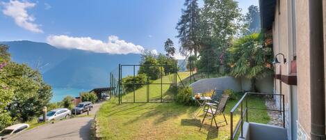 A view of a courtyard with a paved path, a small table with chairs, and a view of the mountains and lake.