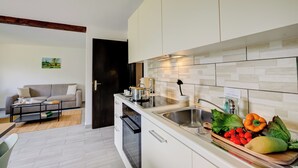 A modern kitchen with white cabinets, a stainless steel sink, and a wooden countertop. There is a dining area with a sofa and a coffee table. - Casa Al Cervo (Lugano)