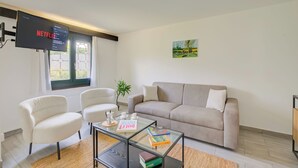 A modern living room with a beige sofa, two white armchairs, a glass coffee table, and a flat-screen TV displaying Netflix. - Casa Al Cervo (Lugano)