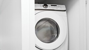 Une machine à laver et un sèche-linge superposés, dans un espace intérieur aux murs blancs.