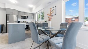 A modern kitchen with stainless steel appliances, a central island, and a dining area with a glass table and blue chairs. - Entire rental unit in Niagara Falls,Free parking (Niagara Falls)
