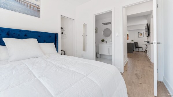 Una habitación de hotel moderna con una cama grande, un cabecero azul, un baño con espejo y vistas a un puente.