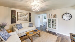Uma sala de estar com um sofá branco, uma mesa de centro de madeira e um relógio de parede grande.