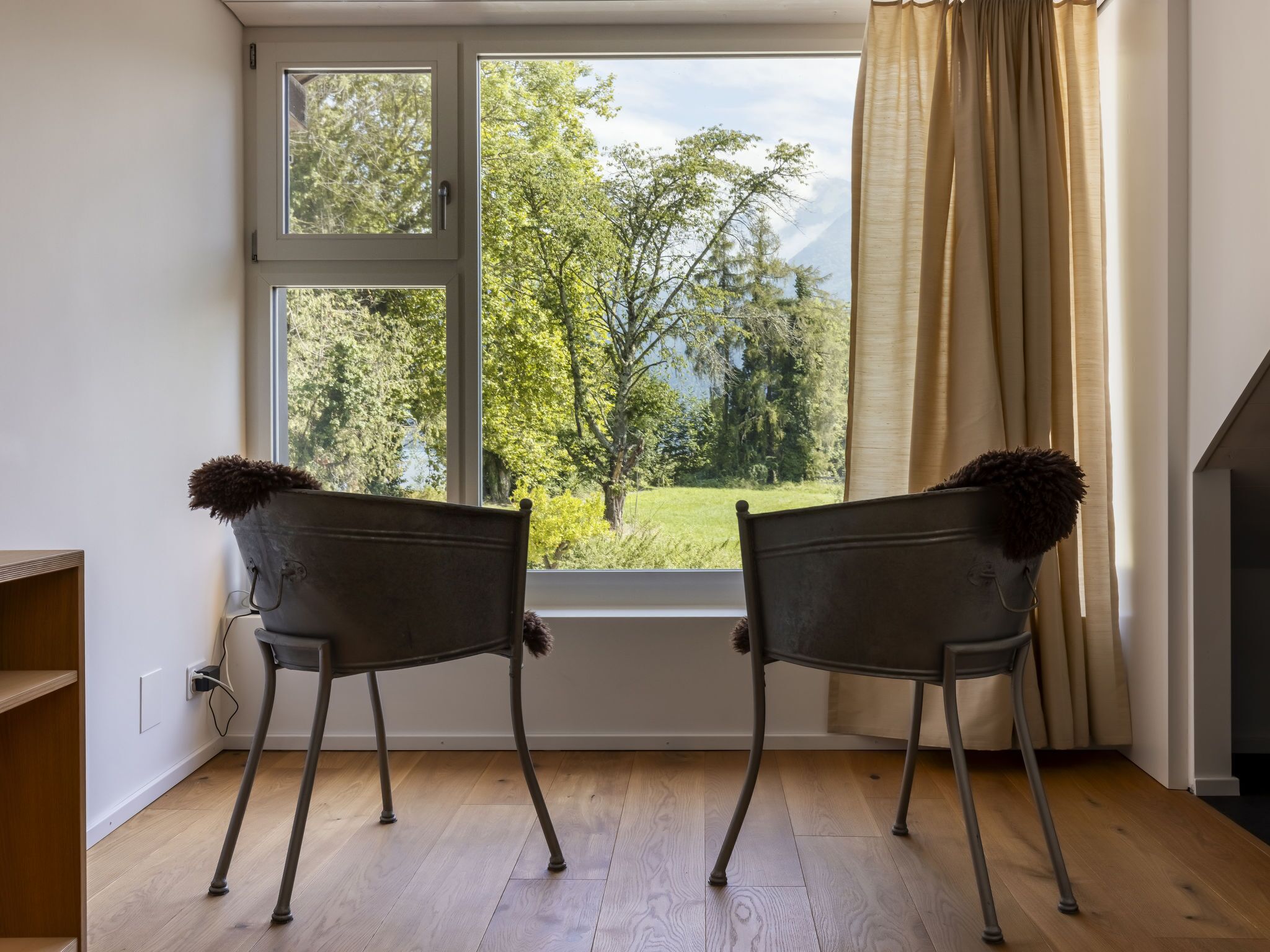 Zwei Stühle vor einem Fenster mit Blick auf Bäume und ein Wiesenfeld.