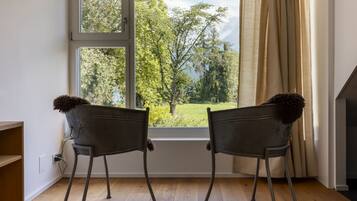 Zwei Stühle vor einem Fenster mit Blick auf Bäume und ein Wiesenfeld.