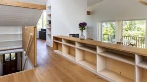 Un intérieur moderne avec un escalier en bois, des étagères intégrées et une grande fenêtre donnant sur l’extérieur.