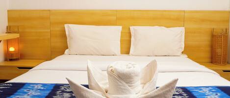 A hotel room with a wooden headboard, white bedding, and a towel art centerpiece on the bed.