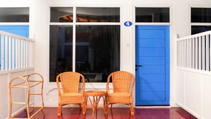 Ein Zimmer mit einer blauen Tür, einem Fenster mit der Nummer 4 und zwei Korbstühlen mit einem kleinen Tisch.