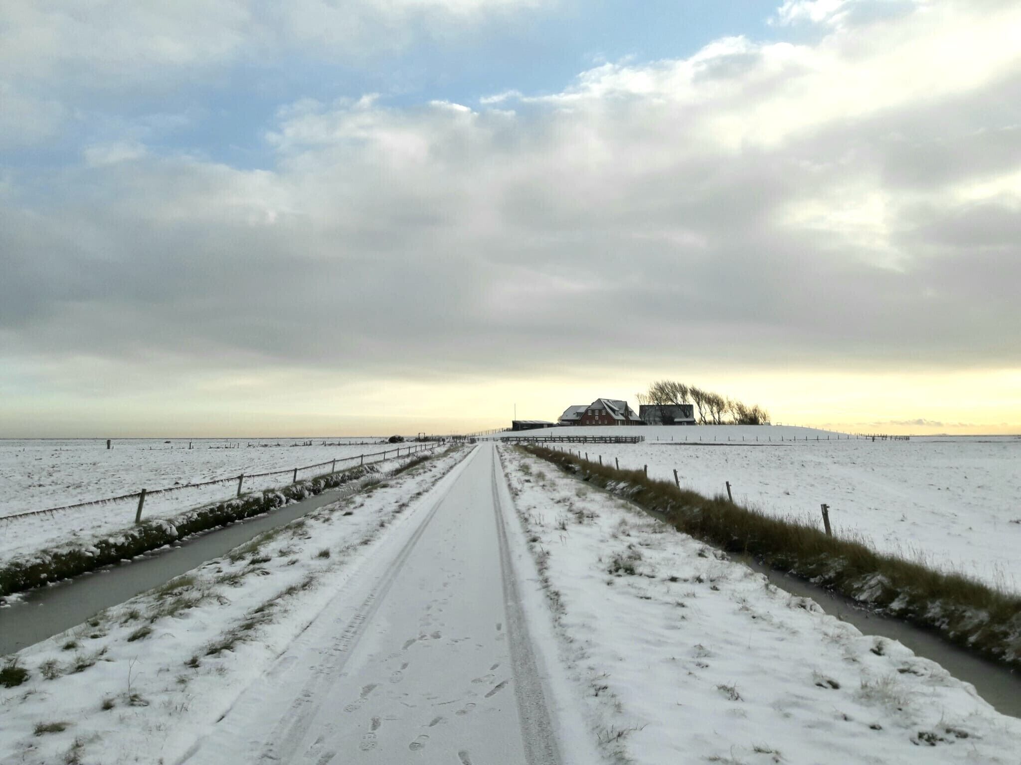 A rural road leading to a farmhouse with a snow-covered landscape.