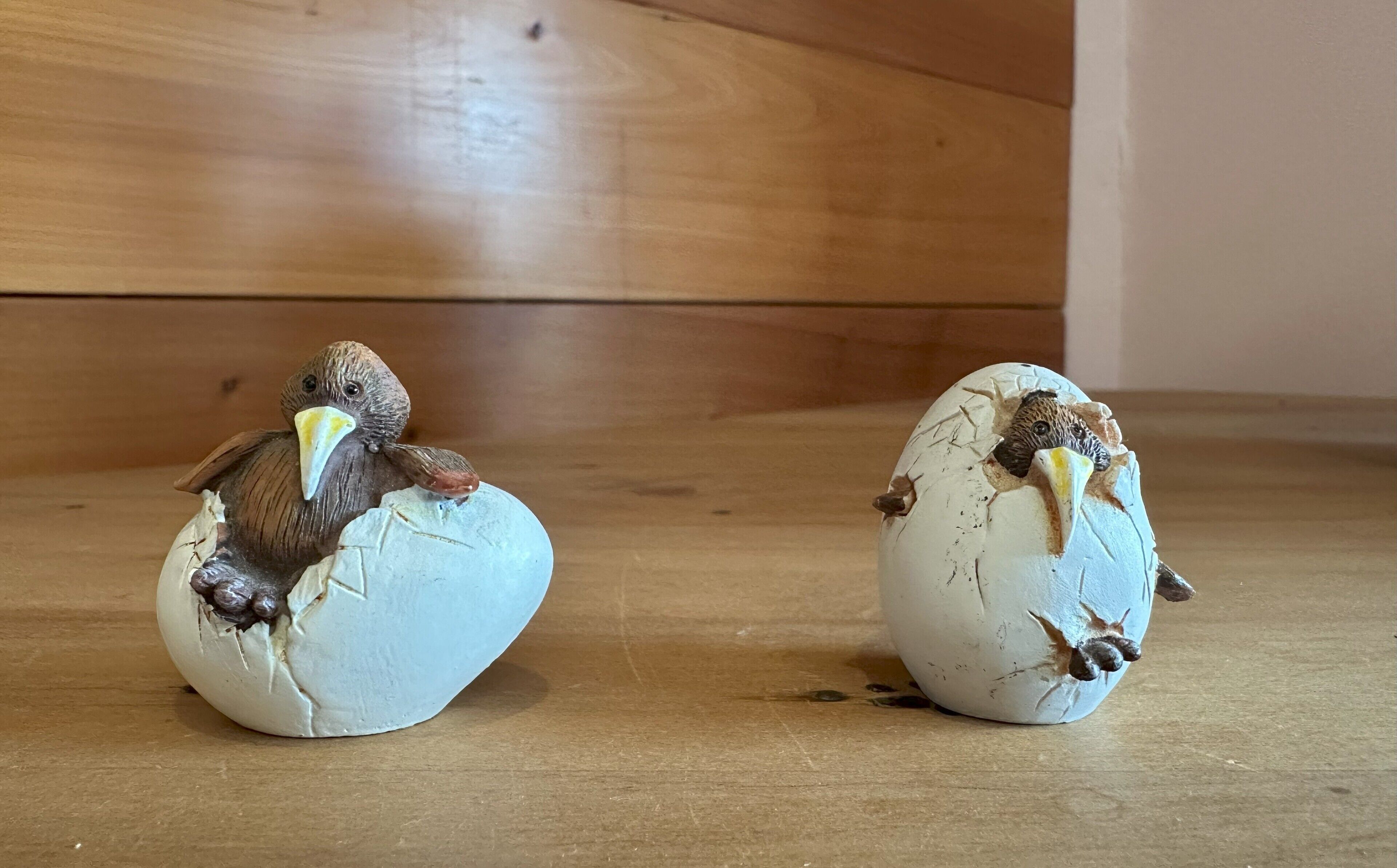 Two ceramic bird sculptures on eggshells placed on a wooden floor.