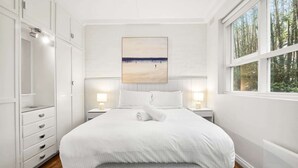 Une chambre à coucher avec un grand lit, deux tables de chevet avec des lampes, une armoire et une fenêtre donnant sur des arbres.