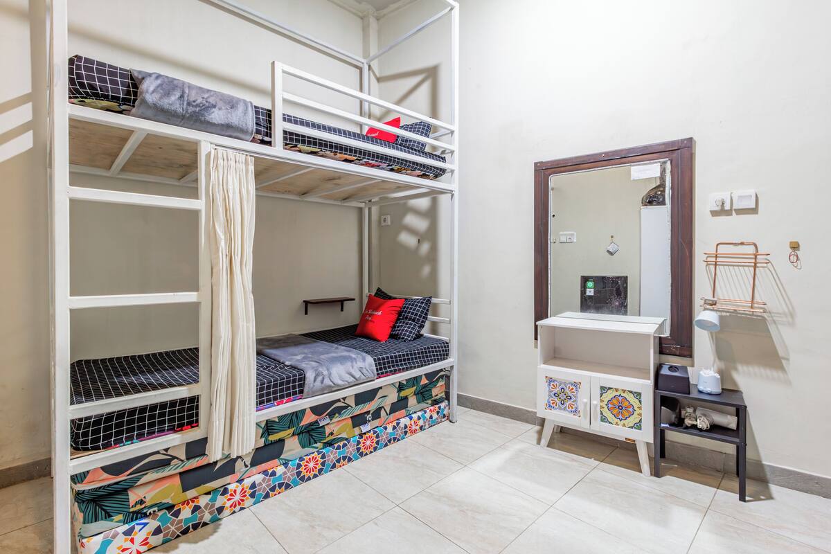 A bunk bed with multiple levels, a small bedside table with a lamp, and a decorative cabinet with tiles.