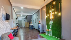 A modern hotel lobby with a wooden floor, a seating area with a red cushion, a green wall with a neon sign, and a staircase in the background. - Collection O Seminyak Near Seminyak Beach Formerly De Shabach (Legian)