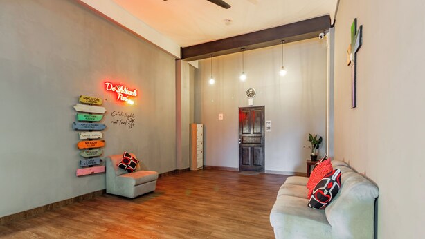 A spacious living area with a wooden floor, a grey sofa with a red and black pillow, and a neon sign on the wall. - Collection O Seminyak Near Seminyak Beach Formerly De Shabach (Legian)