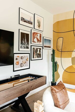 A living room with a TV, a foosball table, a cactus, and framed pictures on the wall. - A Desert Dream | Perfect Getaway in Old Town! (Scottsdale)