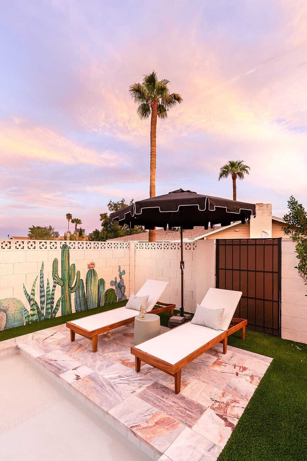 Un patio con dos sillones de descanso, una mesa pequeña y un mural de cactus en la pared.