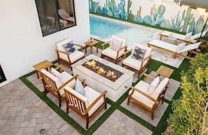 A poolside seating area with a fire pit, surrounded by lounge chairs and a cactus-themed mural.