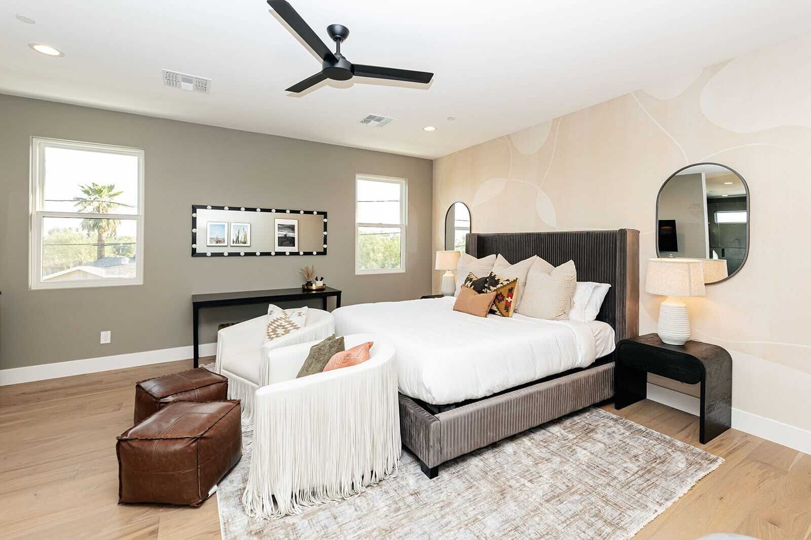 A modern bedroom with a large bed, a ceiling fan, a vanity with a mirror, and a seating area with a bench.