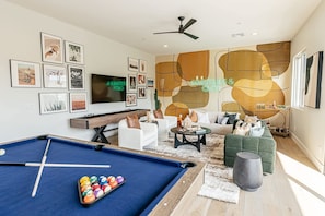 A modern living room with a pool table, a sofa set, a television, and a wall with abstract art.