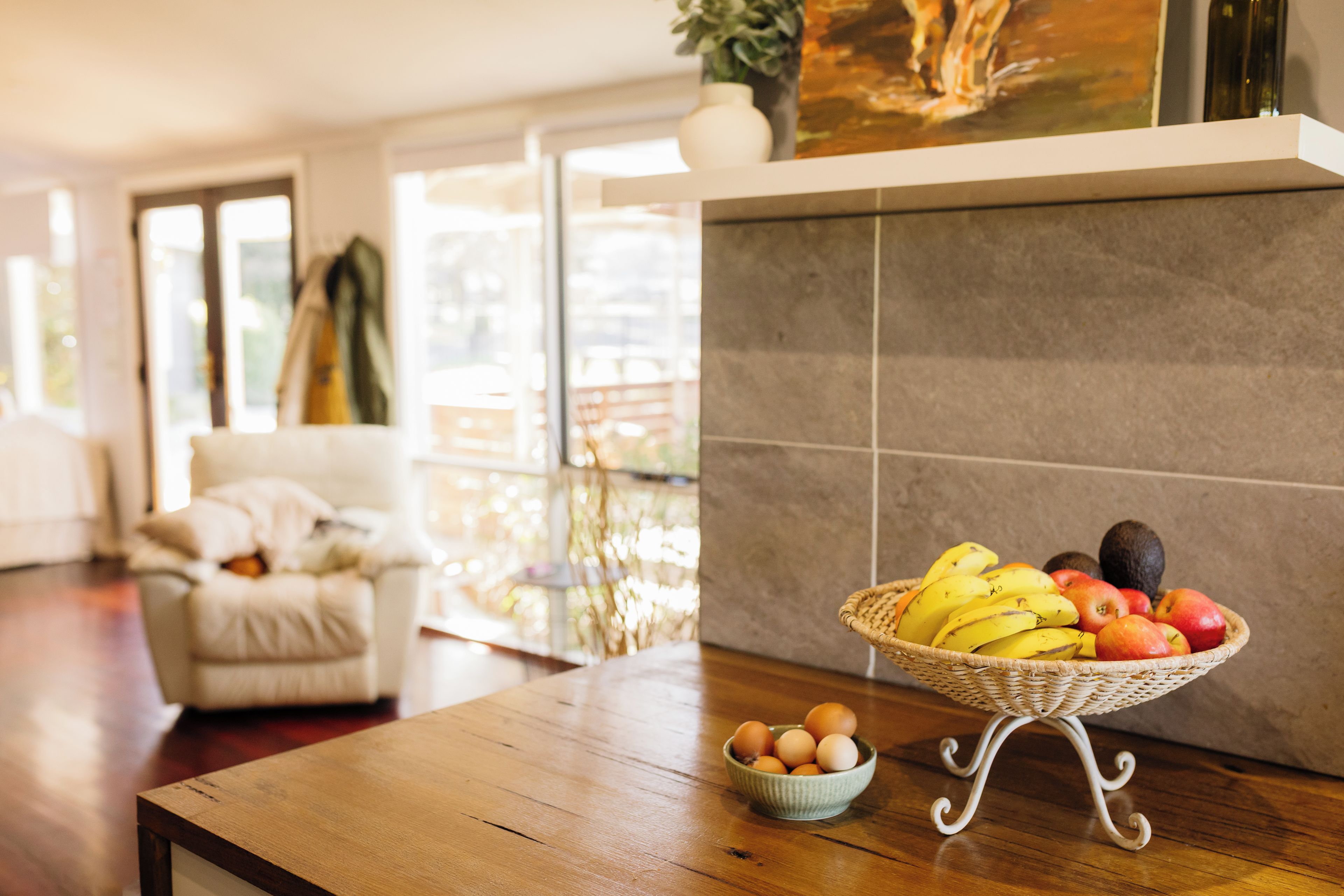 Une pièce avec une table en bois, un panier en osier rempli de fruits et un bol d’œufs.