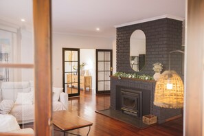 A modern living room with a fireplace, a sofa, a coffee table, and a large mirror on the wall. - Trawalla - an entire house & pool bar - GREAT FOR GROUPS (Gundaroo)