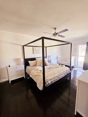 A four-poster bed with a ceiling fan, a bedside table, and a window with curtains.