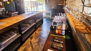 A rustic bar area with wooden tables, a long counter with glasses, and a view of the outside. - Trawalla - an entire house & pool bar - GREAT FOR GROUPS (Gundaroo)
