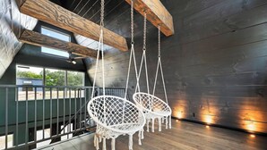 Um quarto com teto inclinado, vigas de madeira e duas cadeiras brancas de macramé penduradas.