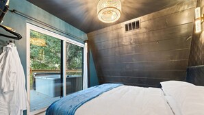 Quarto com cama, janela com vista para uma banheira de hidromassagem e vegetação, e luminária no teto.