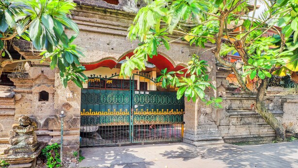 A traditional temple entrance with a stone gate, a stone lion statue, and a tree in the foreground. - Hotel O Danawa House  (Denpasar)