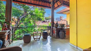 A balcony with a view of a tropical garden, a wooden table, and a decorative urn. - Hotel O Danawa House  (Denpasar)