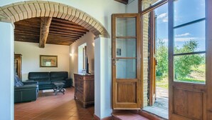 Un salón amplio con puerta de madera que da a un balcón, un sofá de cuero negro y un mueble de madera.