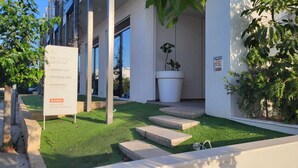 A sign for Mythical Resort with a modern building, a café, gym, and a large planter. - Mythical Sands- HANA (Protaras)