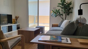 A modern living room with a sofa, a coffee table, a TV, and a large window overlooking a balcony. - Mythical Sands- HANA (Protaras)