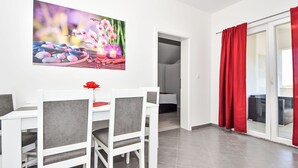 Un comedor con una mesa y sillas blancas, un centro de mesa con flores rojas y un cuadro de flores y rocas en la pared.