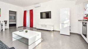 Una sala de estar moderna con un sofá blanco, una mesa de centro de vidrio y un televisor de pantalla plana montado en la pared.