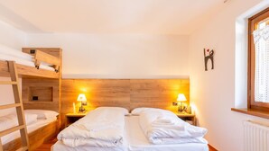 A cozy room with bunk beds, a wooden headboard, two bedside lamps, and a window with a curtain.
